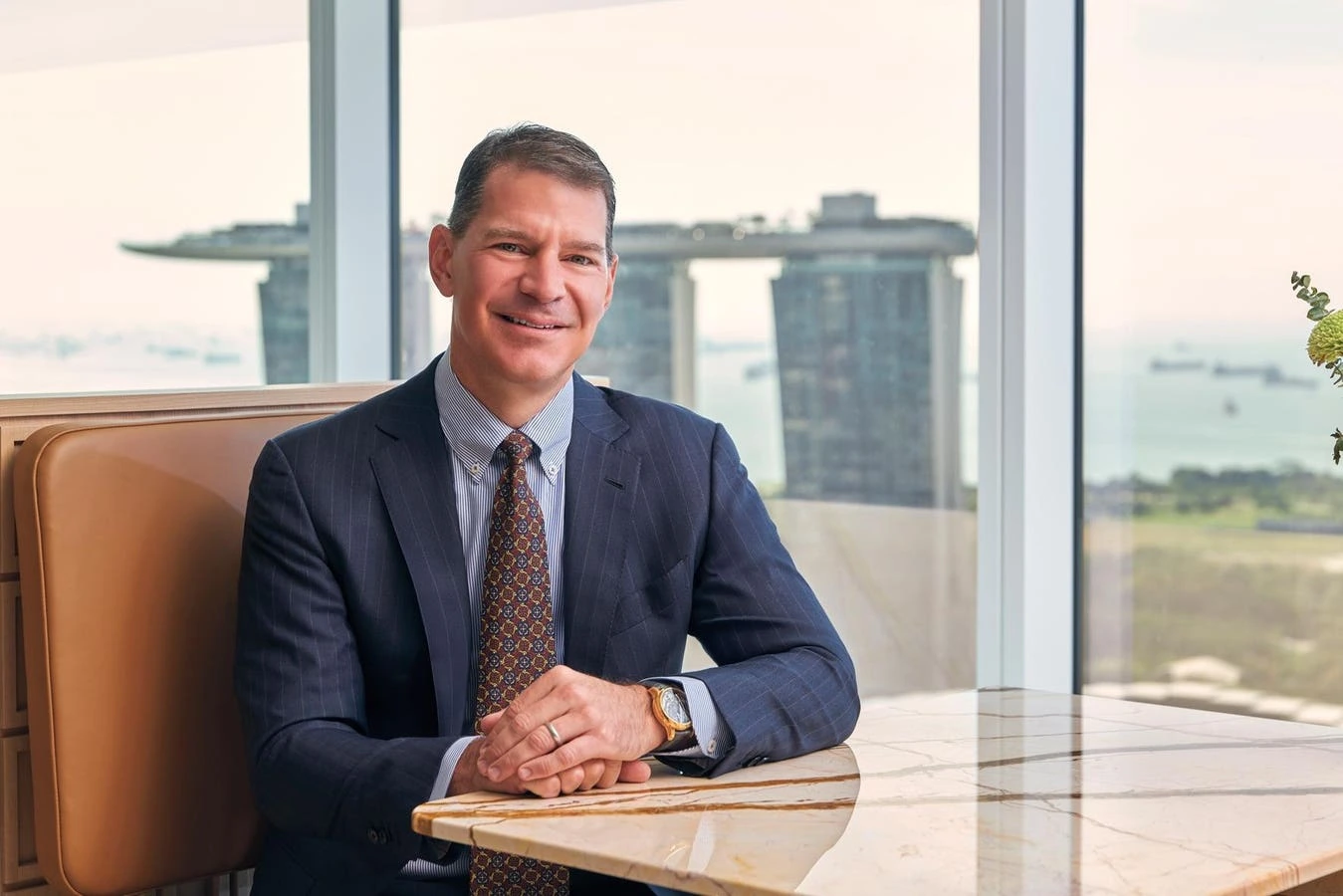 George Pardo seated in a suit at an office table with a city skyline behind him