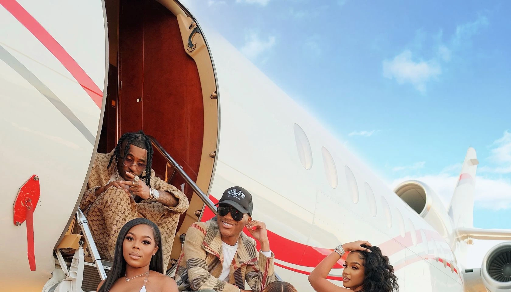 A group of people posing at the open door of a private jet on a sunny day.