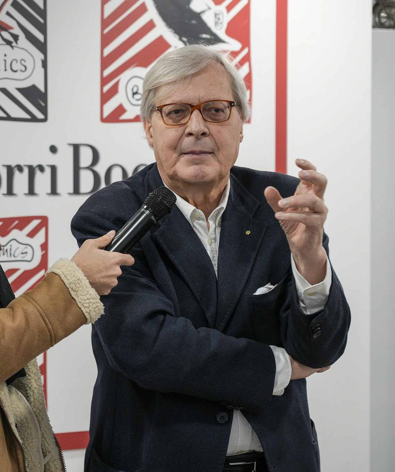 Vittorio Sgarbi speaking at an event with a microphone held toward him