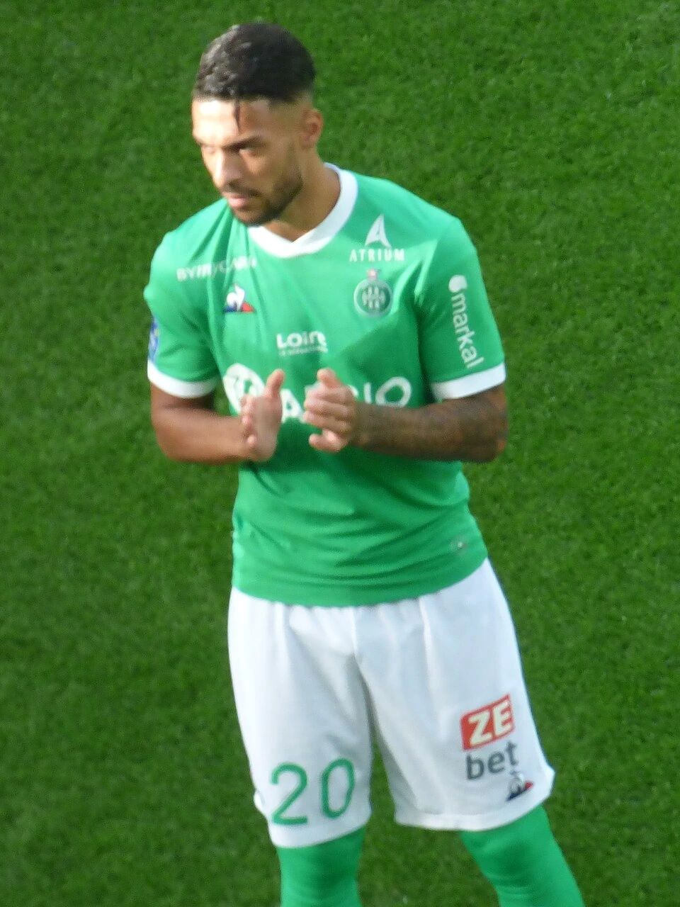 Denis Bouanga in a green Saint-Étienne kit standing on the pitch during a match.