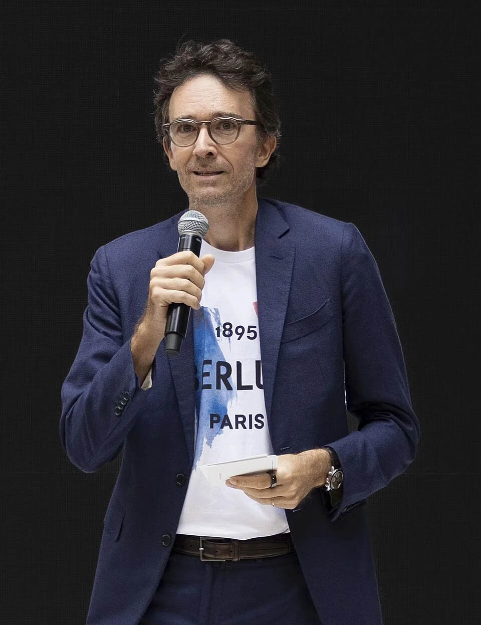 Antoine Arnault speaking at an event, holding a microphone.