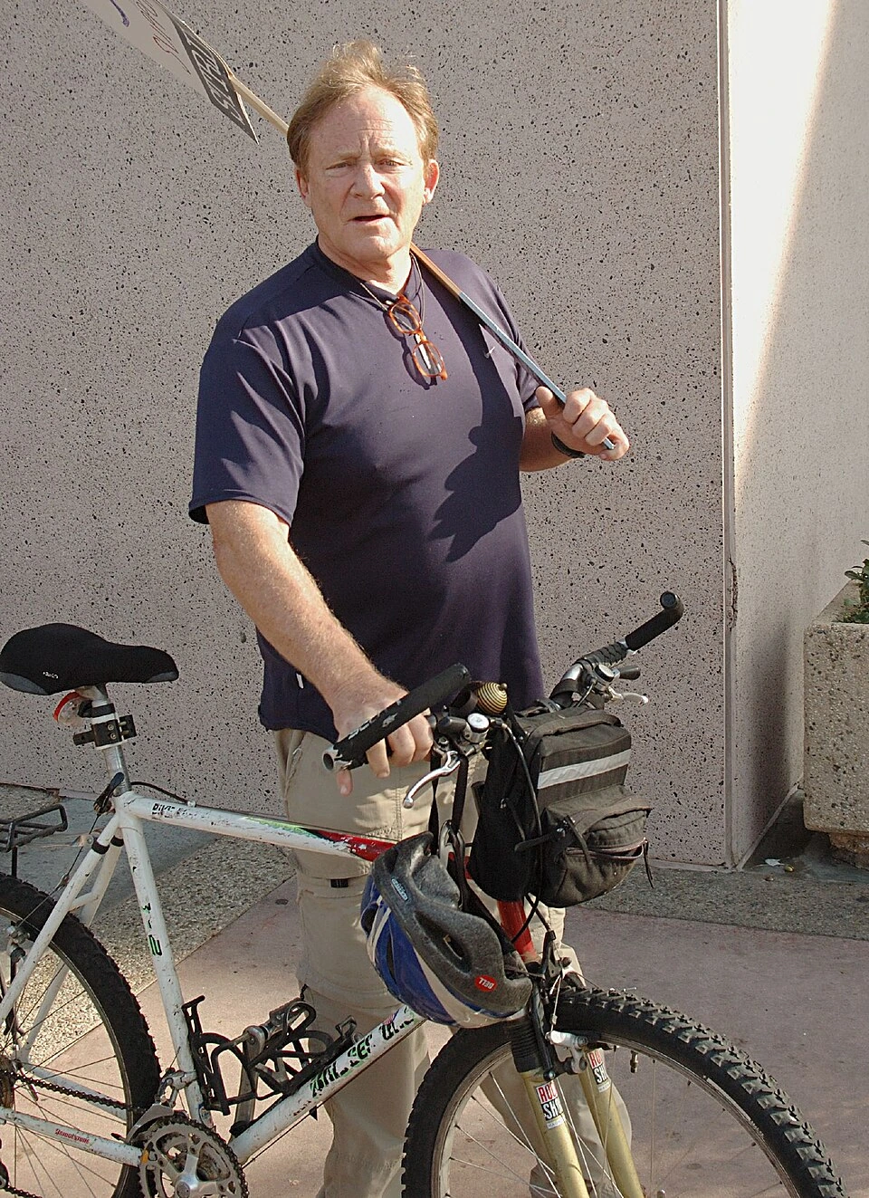 Charles Haid standing beside a bicycle outdoors, wearing a dark shirt and khaki pants.