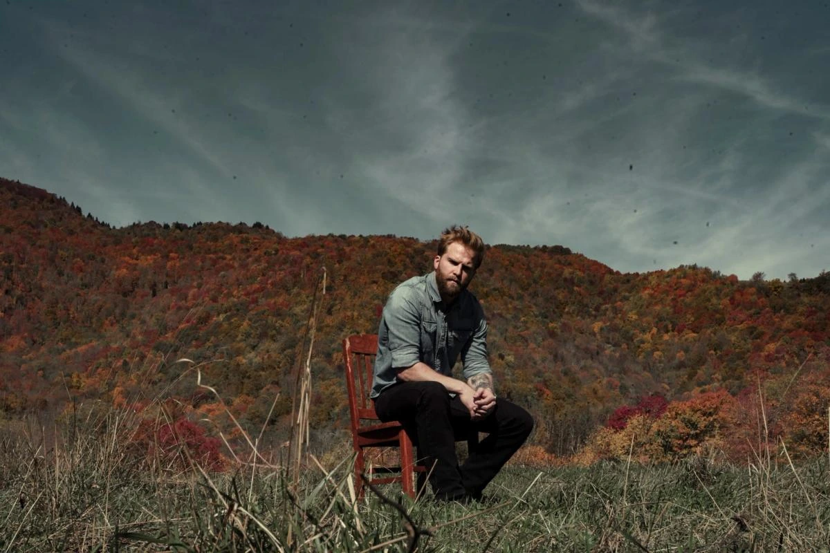Charles Wesley Godwin sitting outdoors on a chair with autumn mountains behind him