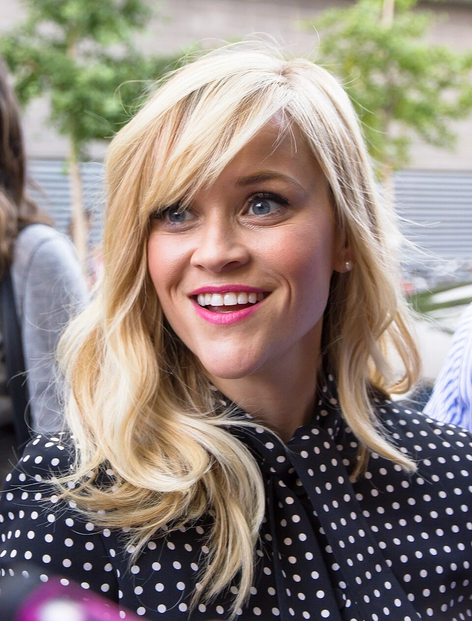 Reese Witherspoon smiling at a public event in a black polka-dot blouse