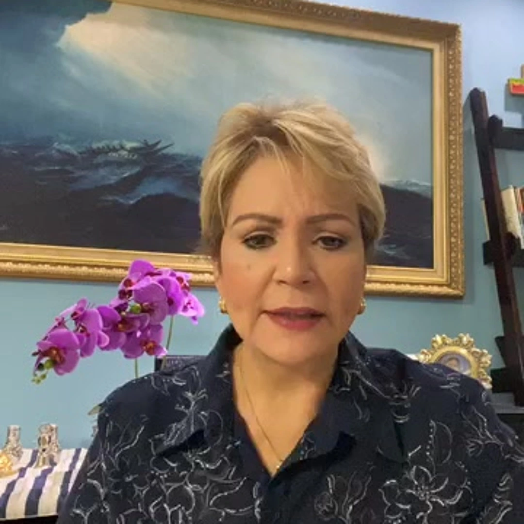 Wanda Rolón speaking on camera indoors in front of framed artwork and flowers