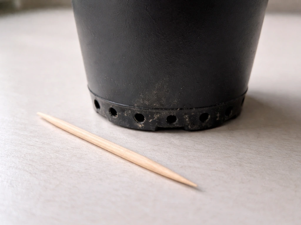 Close-up of a coffee can bottom with several small drainage holes and a toothpick nearby.
