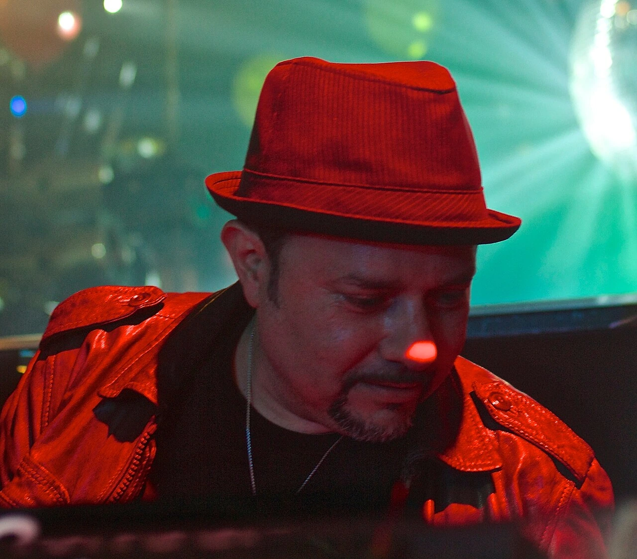 Little Louie Vega performing in a red hat and jacket under club lighting.