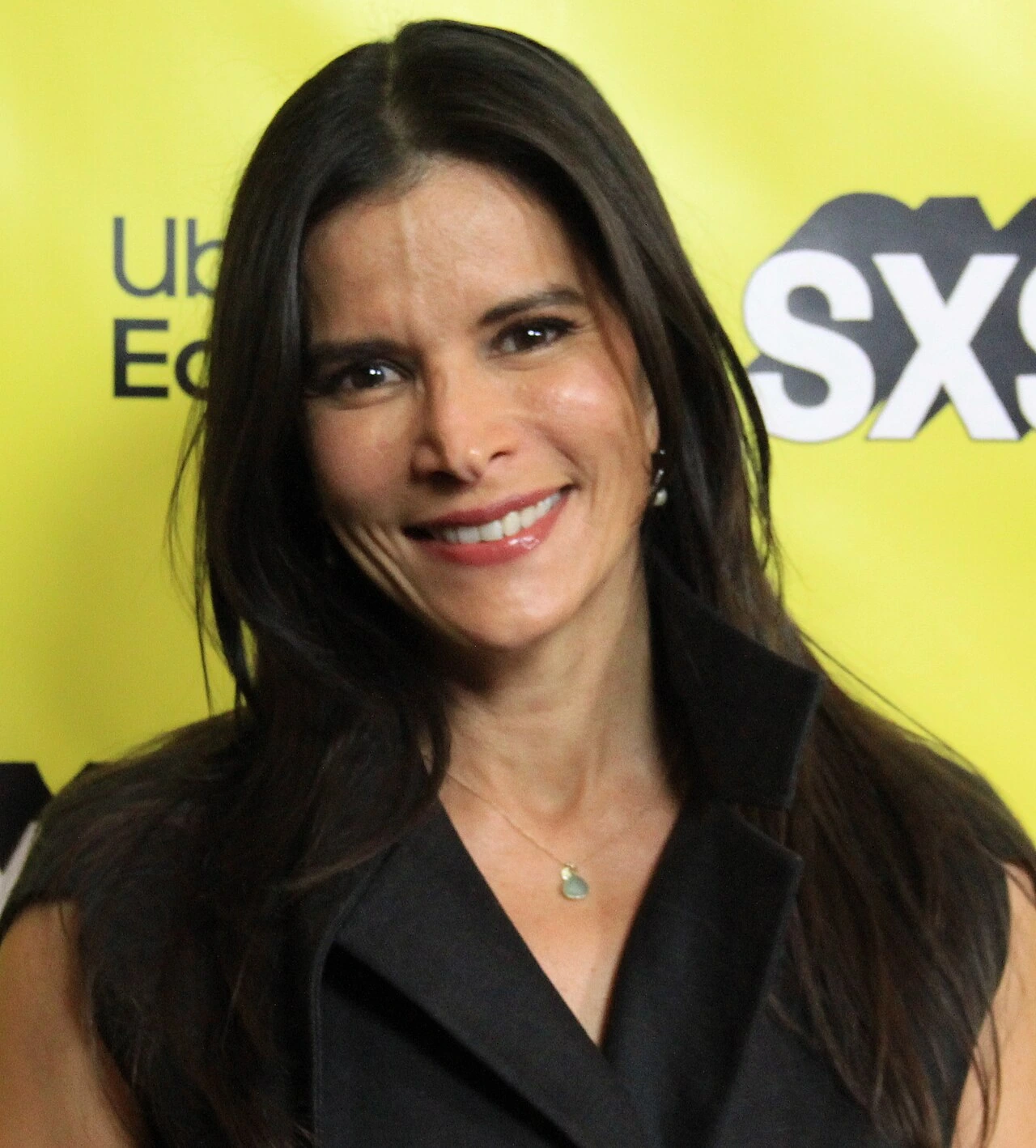 Jaci Velásquez smiling at an event with a yellow backdrop