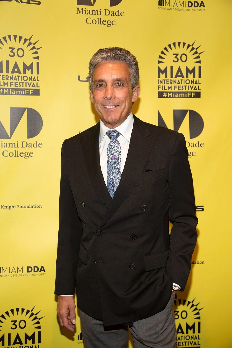 Charles S. Cohen posing at the Miami International Film Festival step-and-repeat backdrop in a suit.
