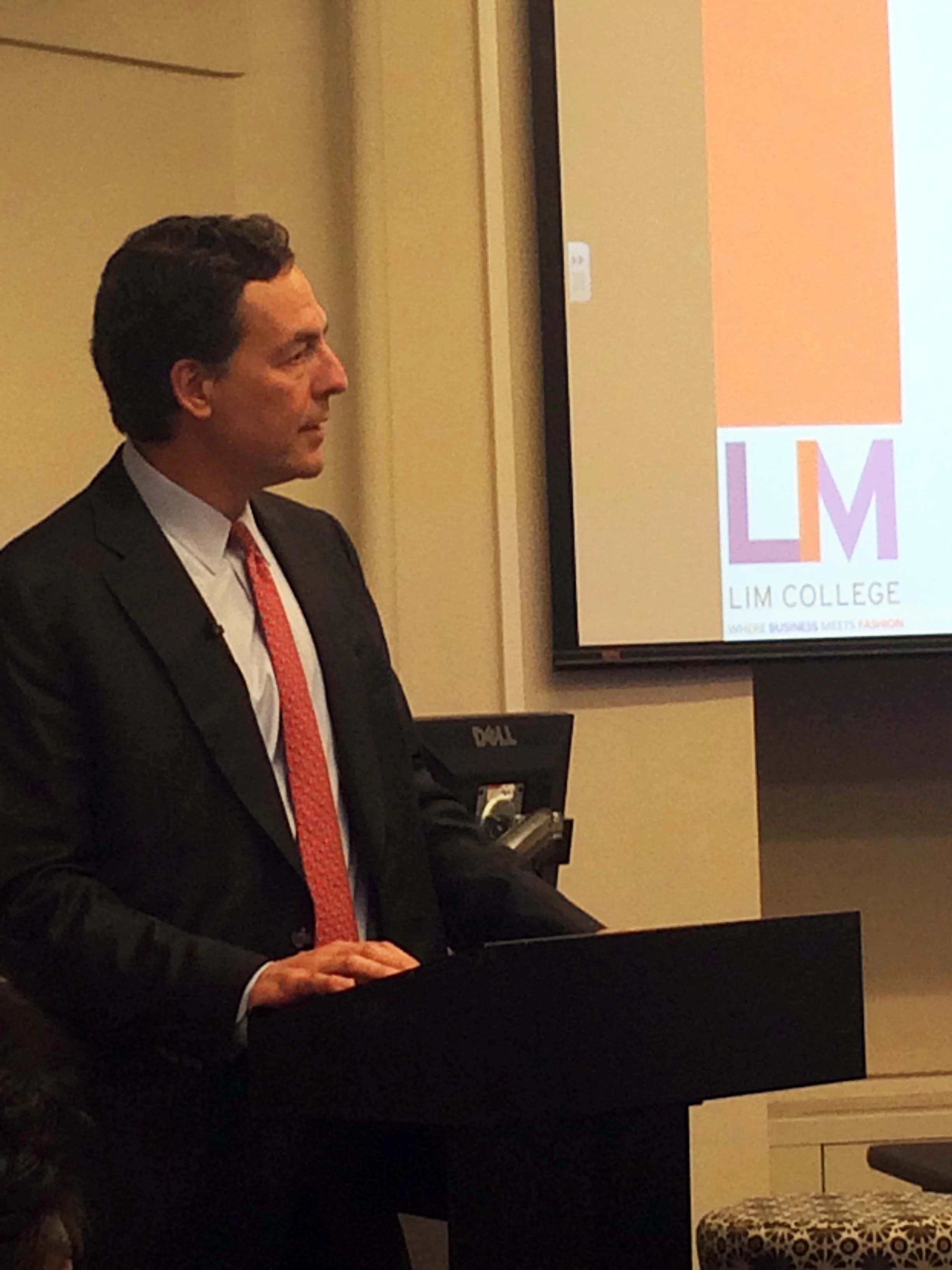 Charles Komar speaking at a podium in a business presentation setting