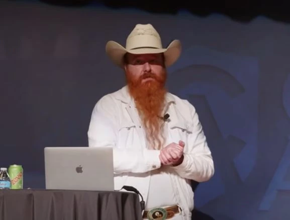 Jimmy Akin speaking on stage at an event, wearing a cowboy hat and white shirt.