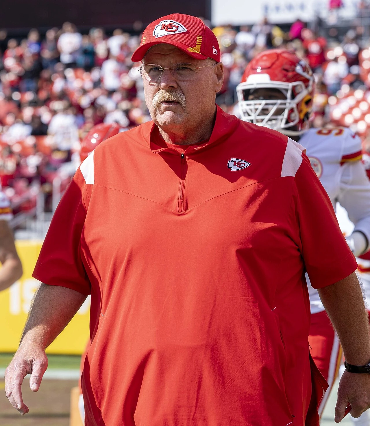 Andy Reid, head coach of the Kansas City Chiefs, on the sideline in a red team shirt and cap during an NFL game.