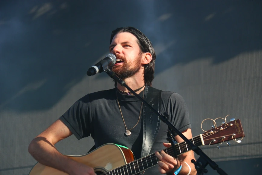 Seth Avett performing on stage with a guitar and microphone