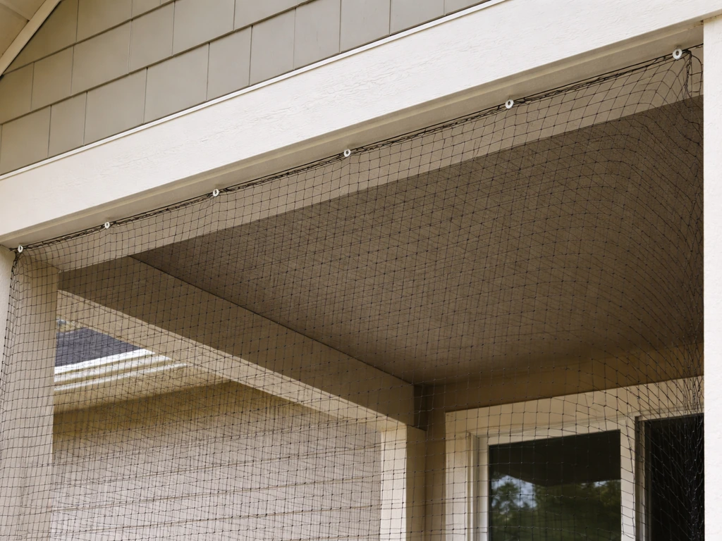 Heavy-duty bird netting installed under eaves, draped over a porch opening with fasteners visible.