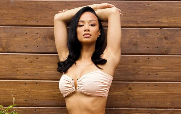 A woman posing in a strapless top against a wooden wall.
