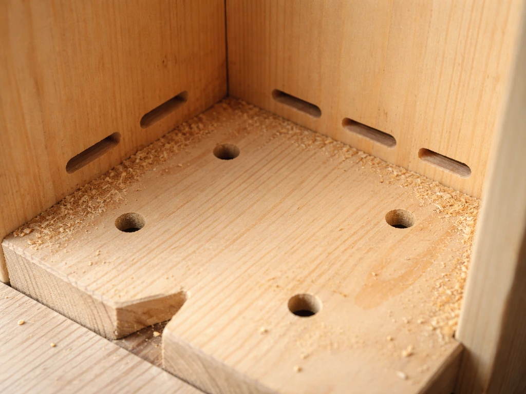Close-up of a wooden structure floor with drilled drainage holes and small side ventilation slots