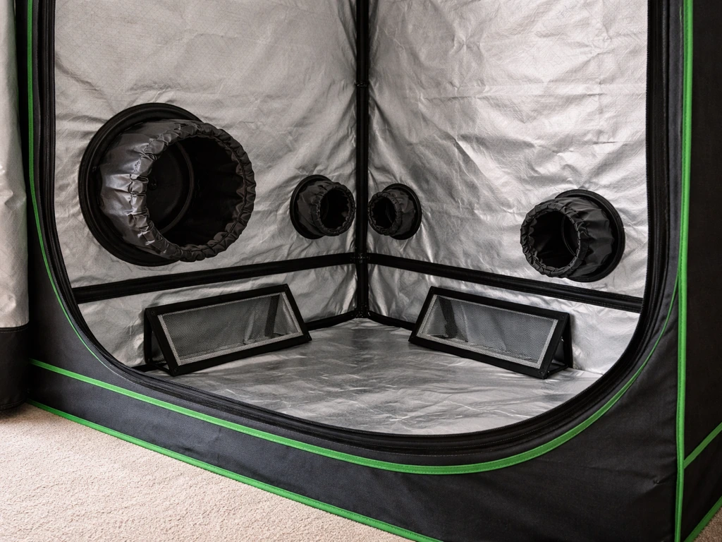 Close-up of a grow tent’s lower duct ports and mesh intake vents with adjustable flaps.