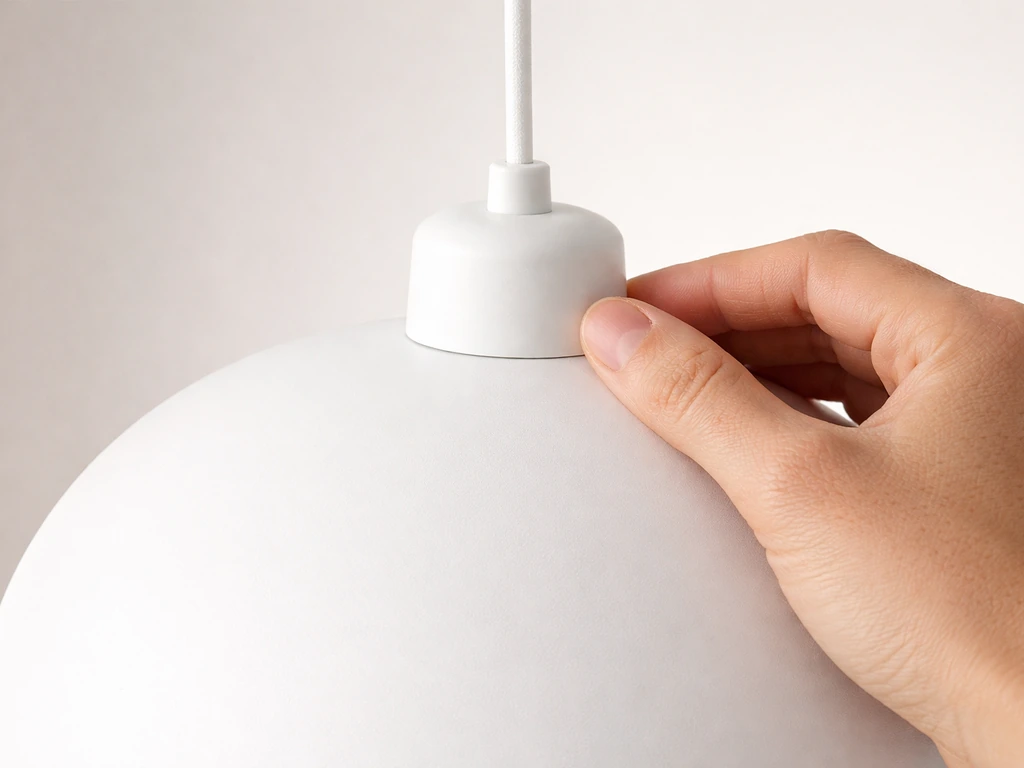Hand inspecting a white pendant light’s housing and cord entry in a clean, minimal room.