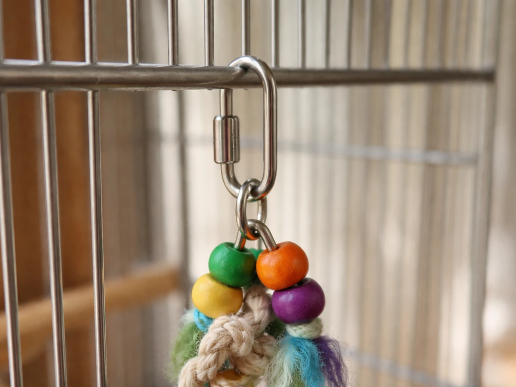 Close-up of a stainless quick link threaded through a cage bar and toy hanging loop, properly closed.