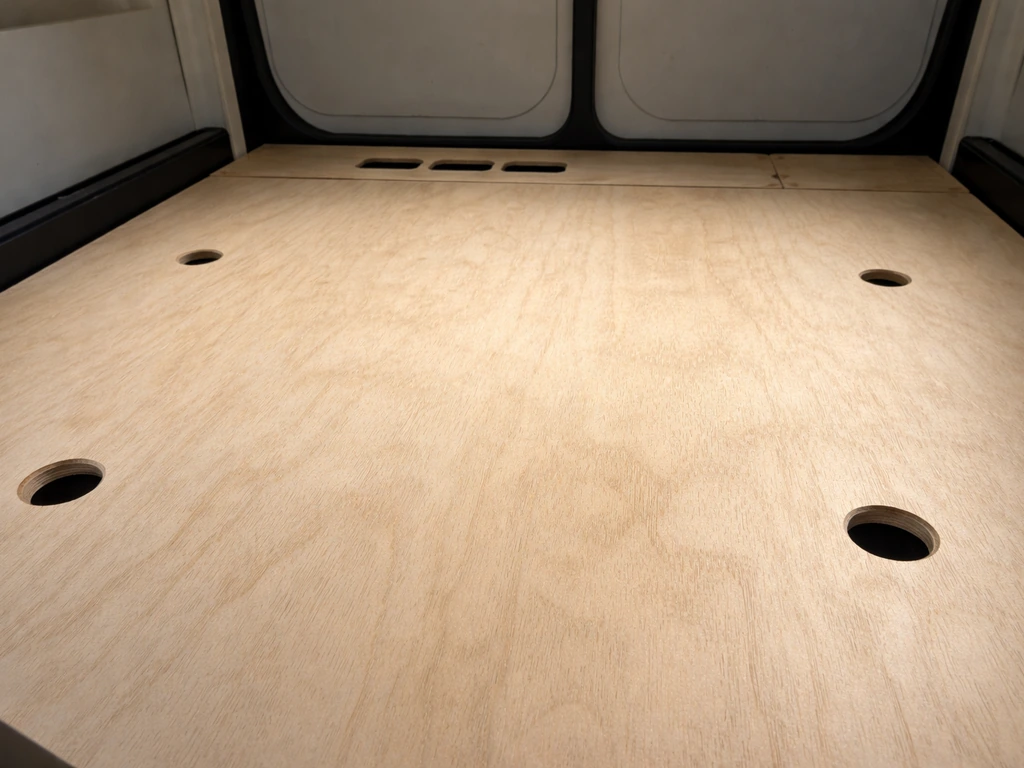 Close-up of a compartment floor panel showing four drilled drainage holes near corners and airflow gaps