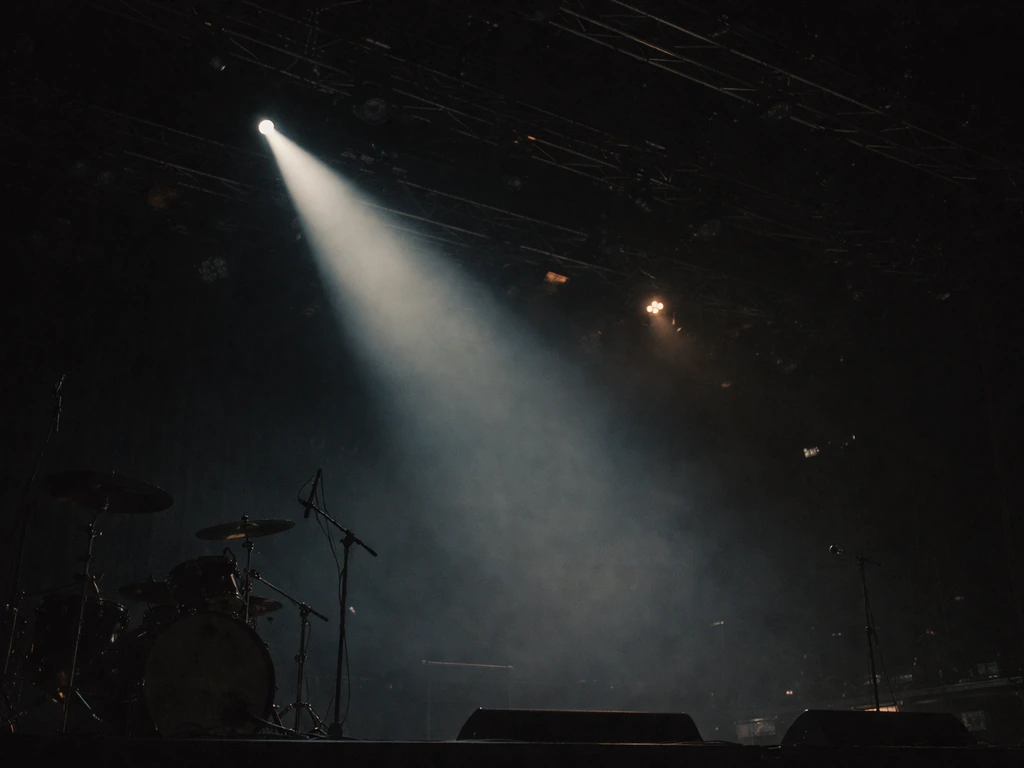 Night concert stage with sweeping spotlight, light haze, and a drum kit silhouette in view