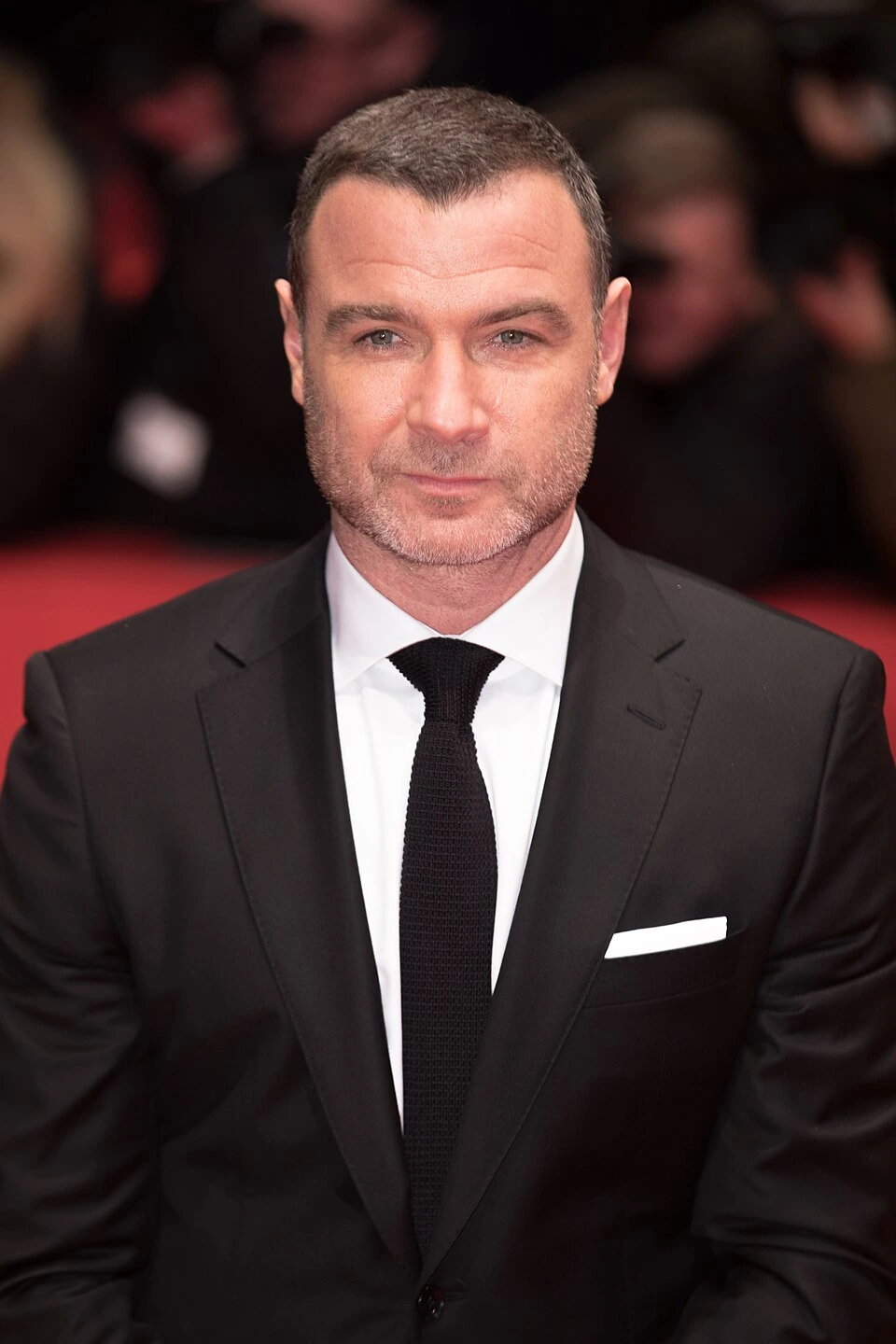 Liev Schreiber at the Berlinale 2018 in a black suit and tie, facing the camera at a red carpet event.