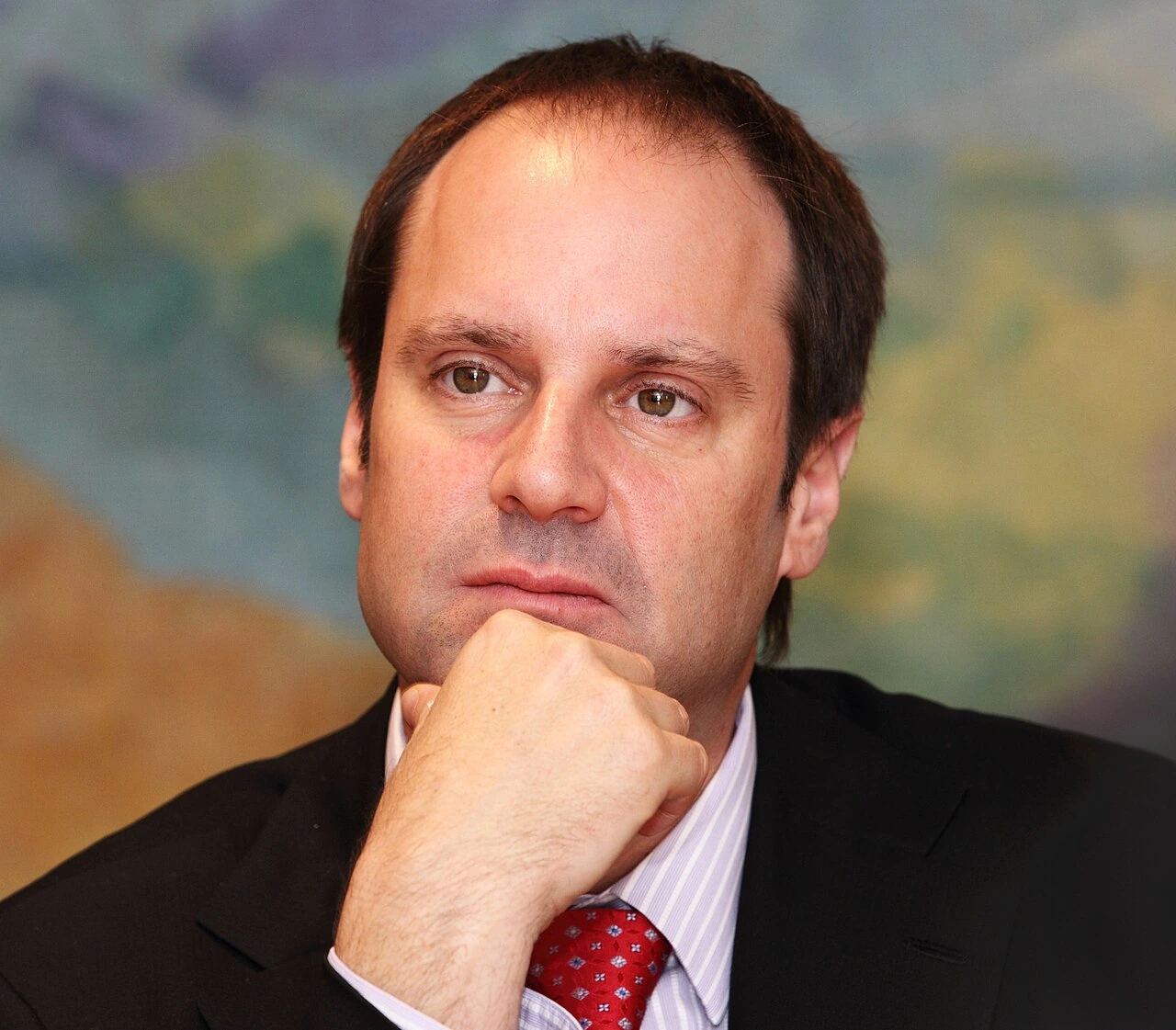 Portrait of Jeffrey Skoll in a suit and tie, resting his chin on his hand against a blurred background.
