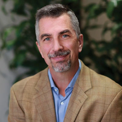 Portrait of Tim Schantz, CEO of Troon, in a tan blazer and blue shirt.