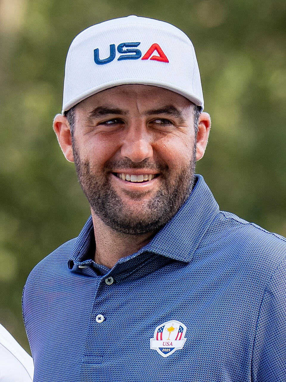 Scottie Scheffler smiling in a USA golf cap and blue shirt at the Ryder Cup
