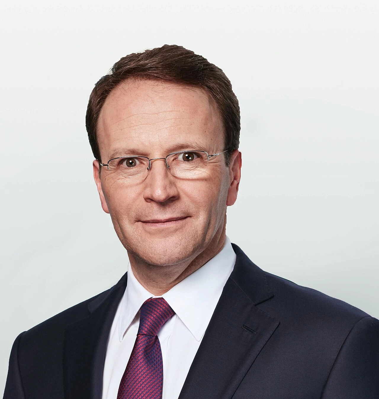 Portrait photo of Ulf Mark Schneider in a suit and tie against a plain light background.