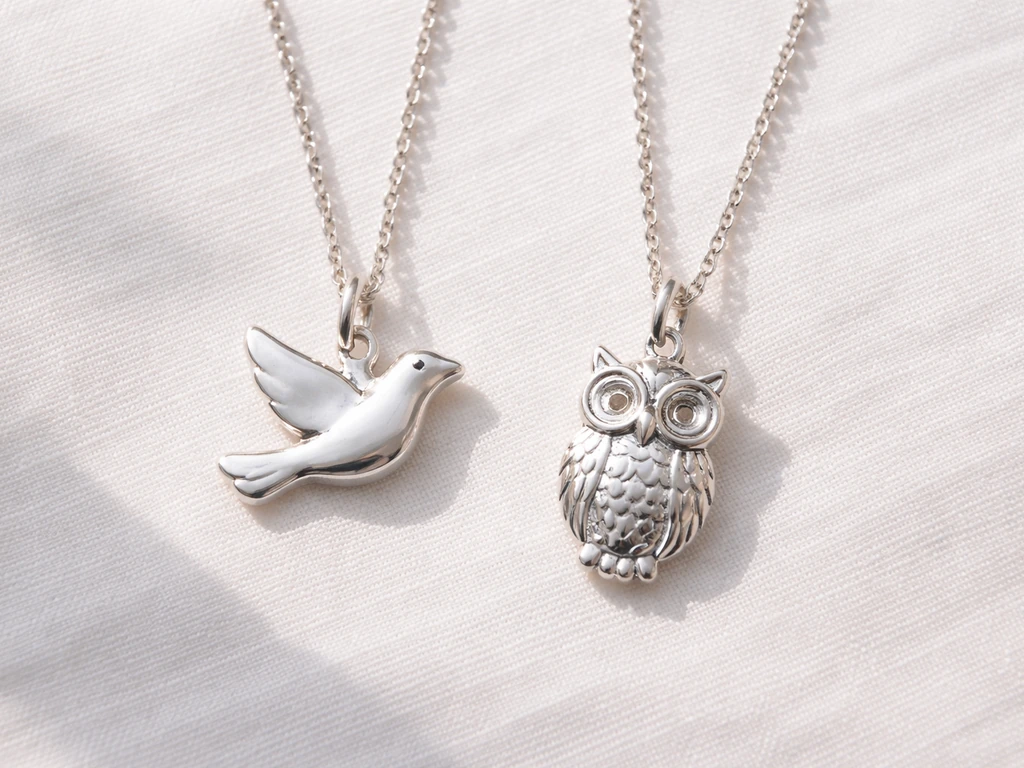 Side-by-side dove and owl silver bird pendant necklaces on white linen cloth.
