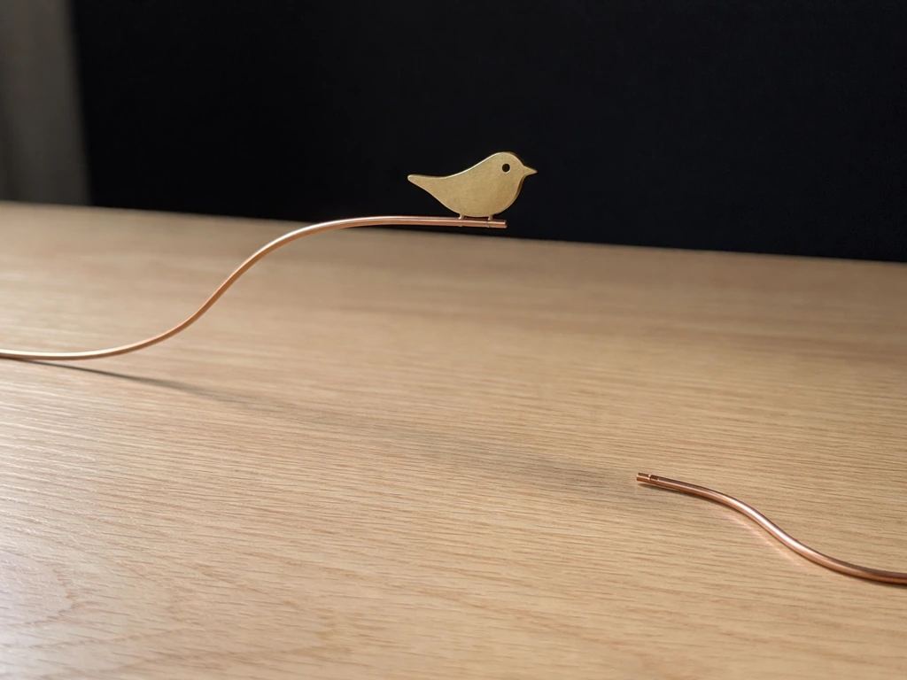 Bird-shaped conductive piece sits on one open copper wire with no return path, showing an incomplete circuit.