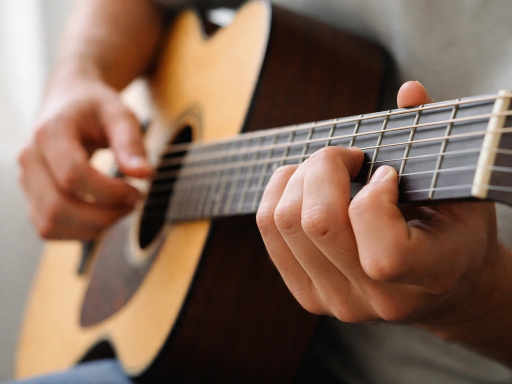 Close-up of guitar fretting hand holding a chord while the other hand strums in natural light.