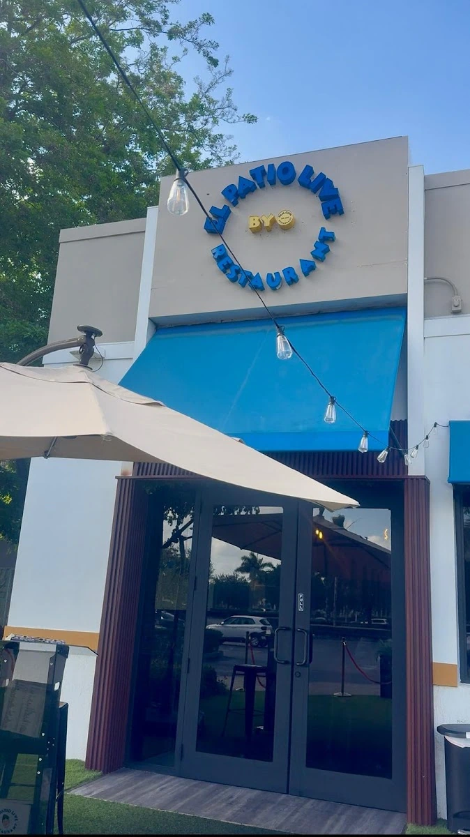 Exterior view of El Patio Live restaurant in Hialeah with patio umbrella and entrance signage.