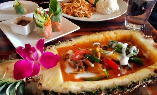 A plated Thai dish served at The Patio Fine Thai Cuisine, with a colorful edible flower garnish and other dishes visible
