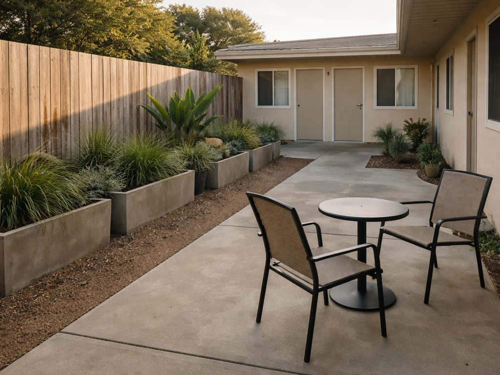 Quiet motel-style outdoor patio courtyard with chairs and a small table under soft daylight.
