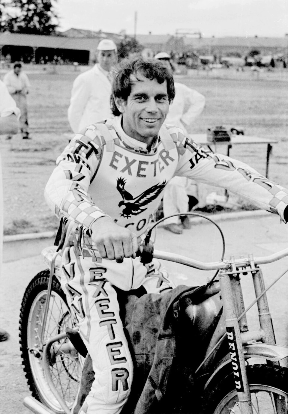 Ivan Mauger seated on a speedway motorcycle, smiling in a black-and-white photo.