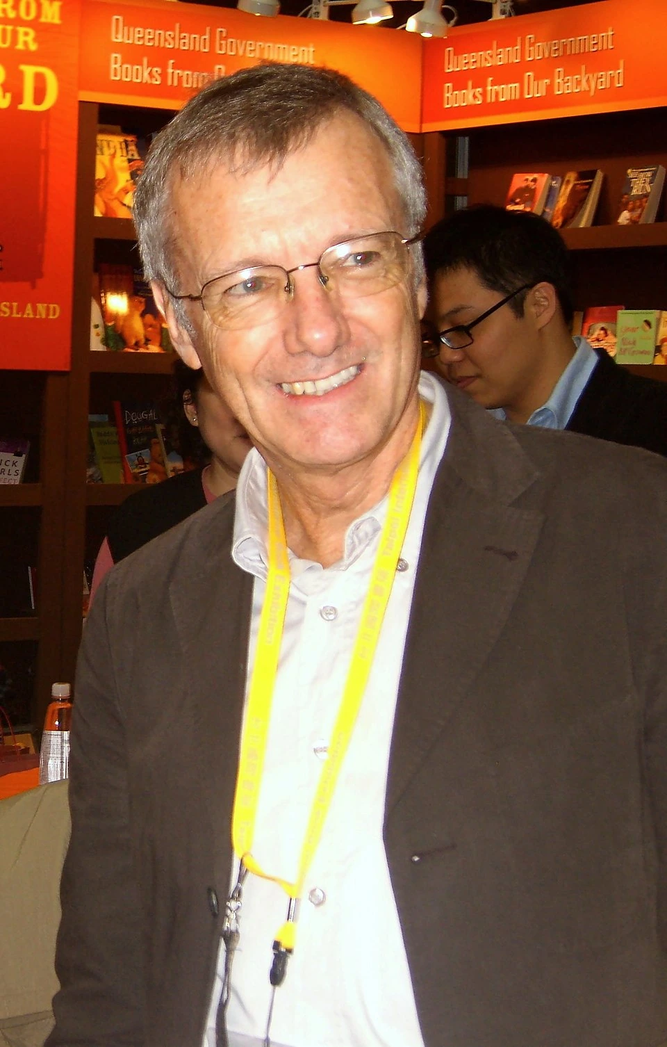 Tony Wheeler smiling at an event, wearing glasses and a lanyard.