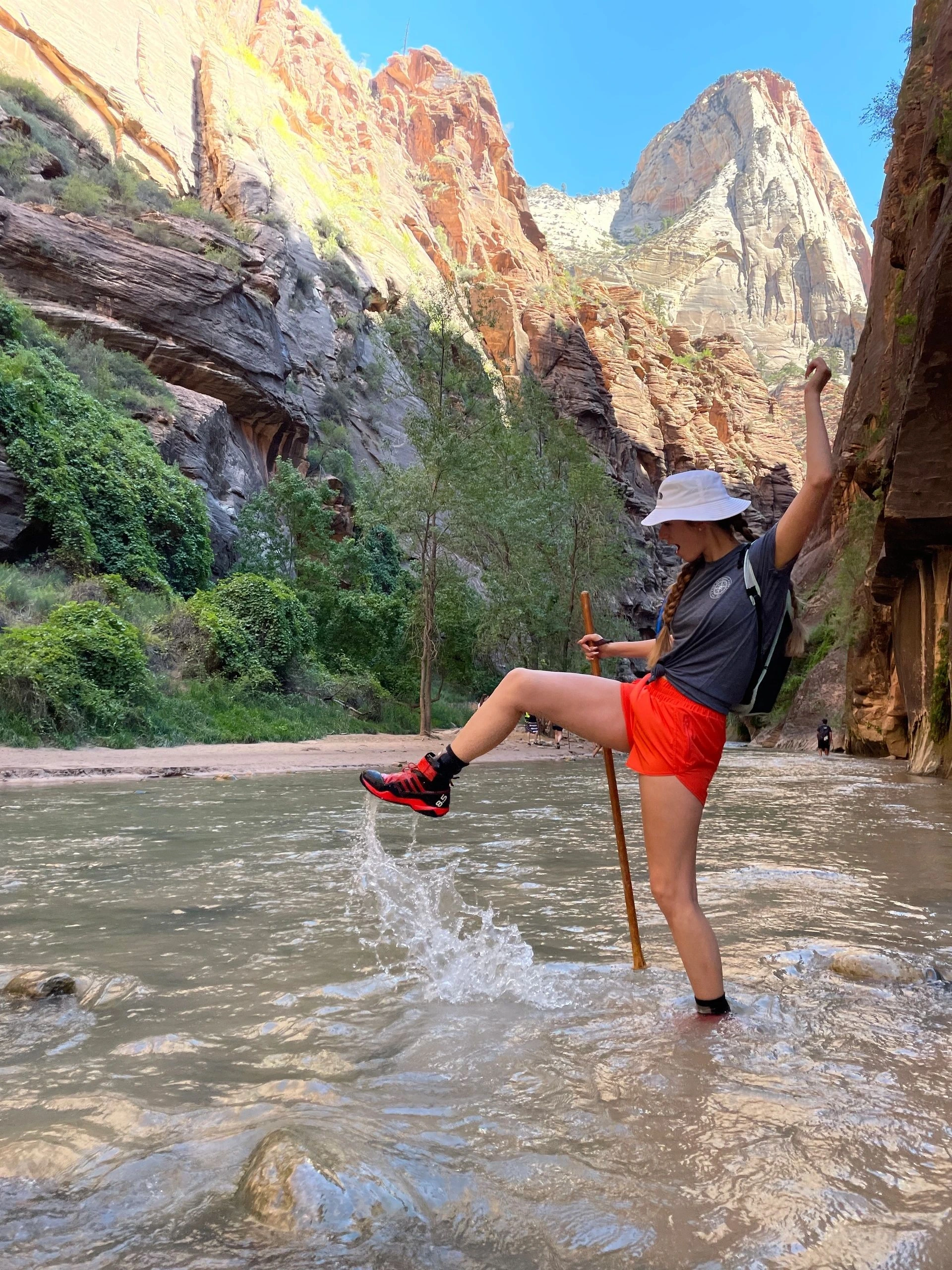 Aubrey Burchell posing outdoors in a canyon stream, wearing a hat and bright shorts.