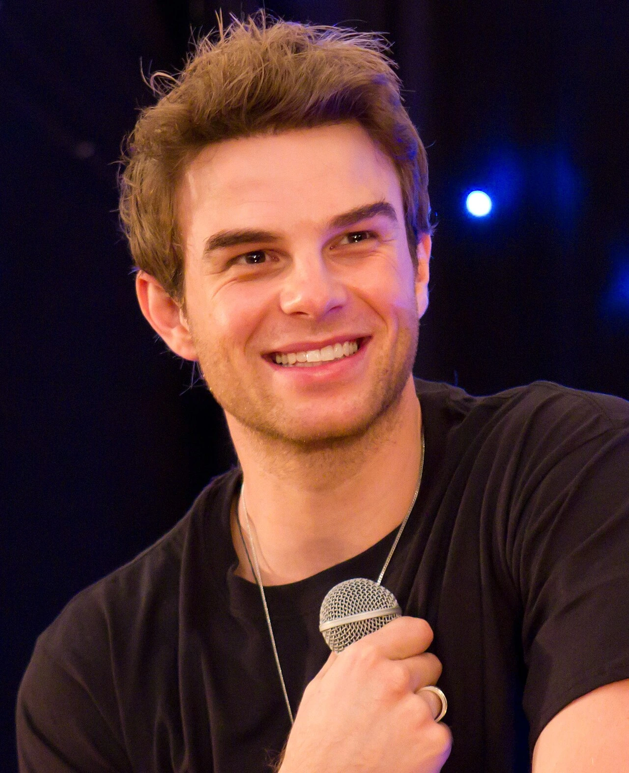 Nathaniel Buzolic smiling while holding a microphone on stage