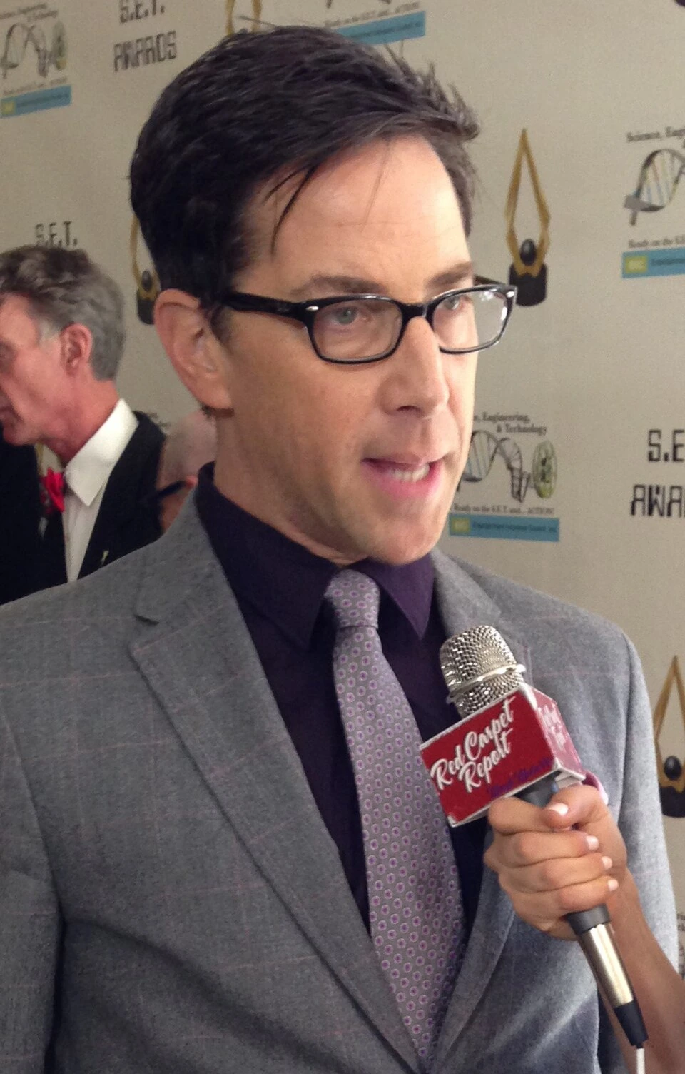 Dan Bucatinsky at an event, wearing glasses and a suit while being interviewed
