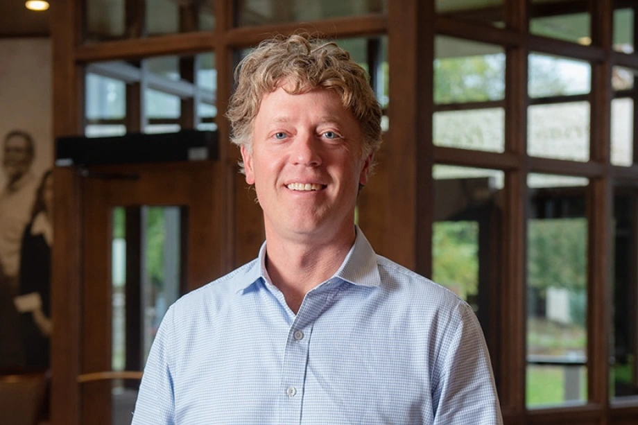 Louie Gentine smiling in a professional indoor portrait, wearing a light blue shirt with a blurred office-like backgroun