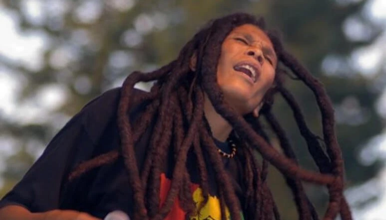 Nasio Fontaine performing outdoors, singing with long dreadlocks visible in a candid music photo