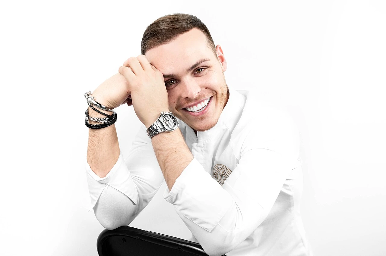 Portrait of Amaury Guichon smiling in a white chef jacket against a white background