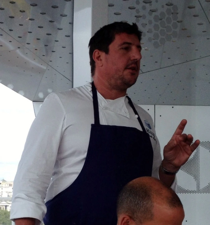Claude Bosi standing in a chef’s apron and white jacket, speaking indoors