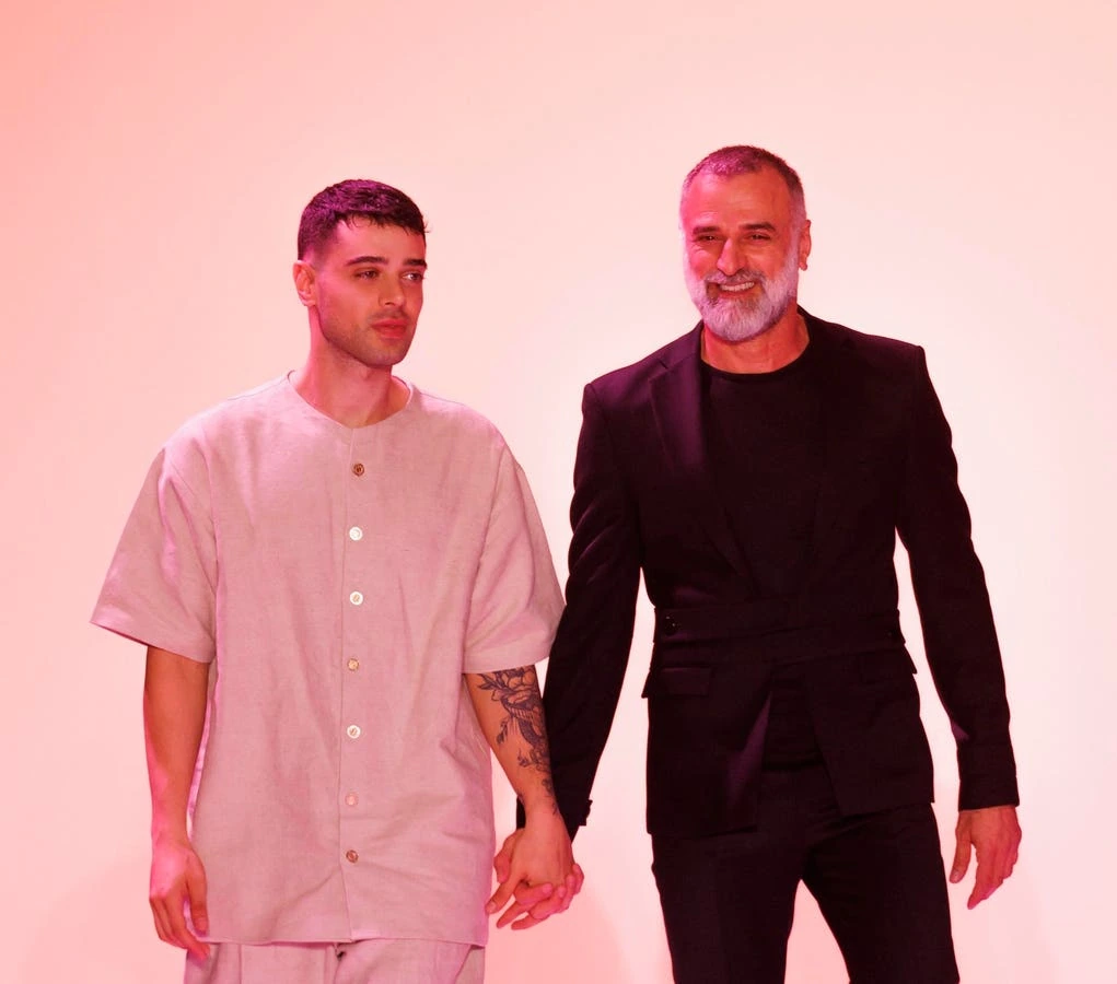 Georges Hobeika at a fashion event, standing beside another model against a pink backdrop