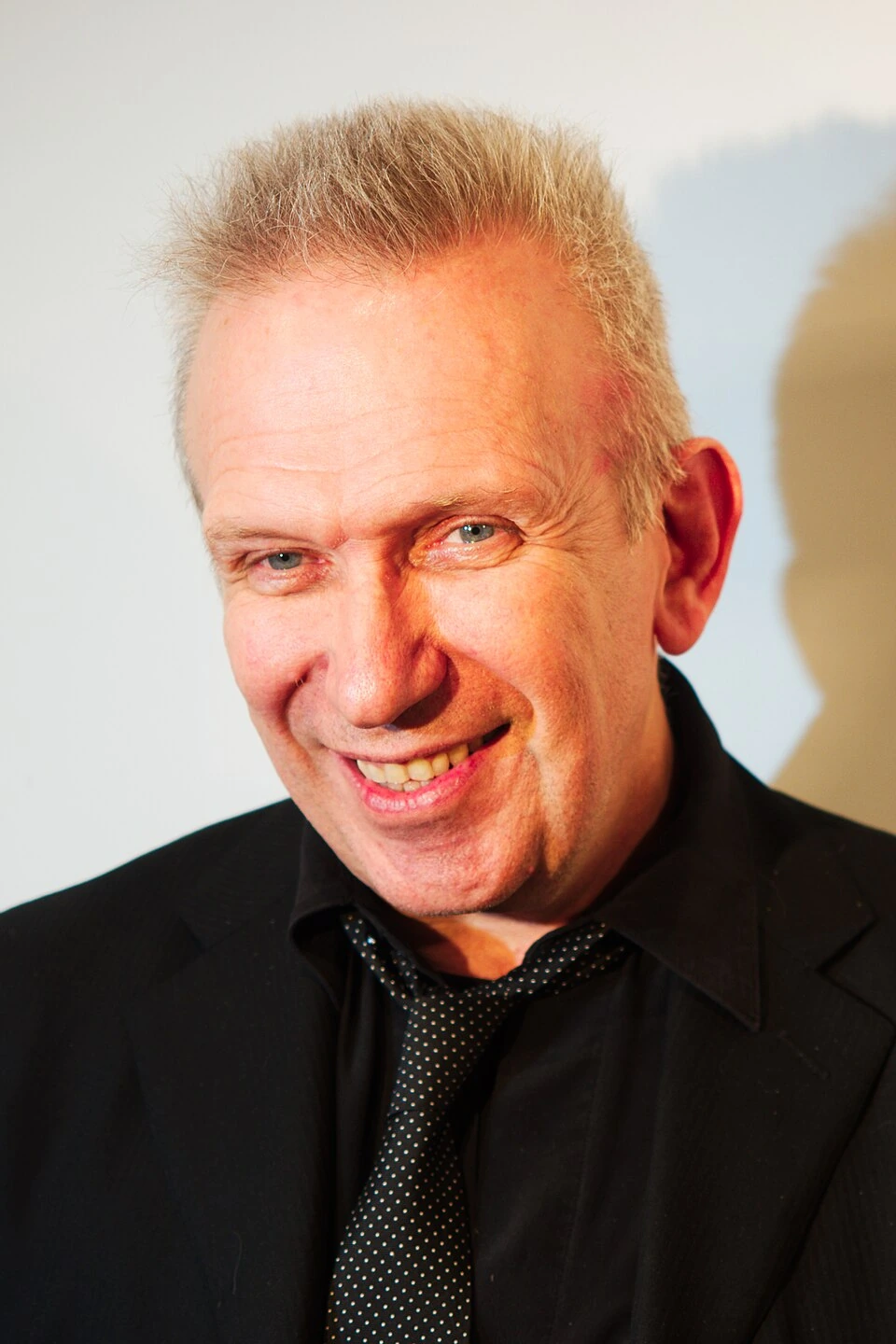Portrait photo of fashion designer Jean Paul Gaultier smiling in a black shirt and tie.