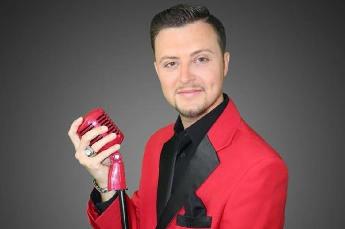 Vinnie Medugno posing in a red jacket holding a vintage microphone
