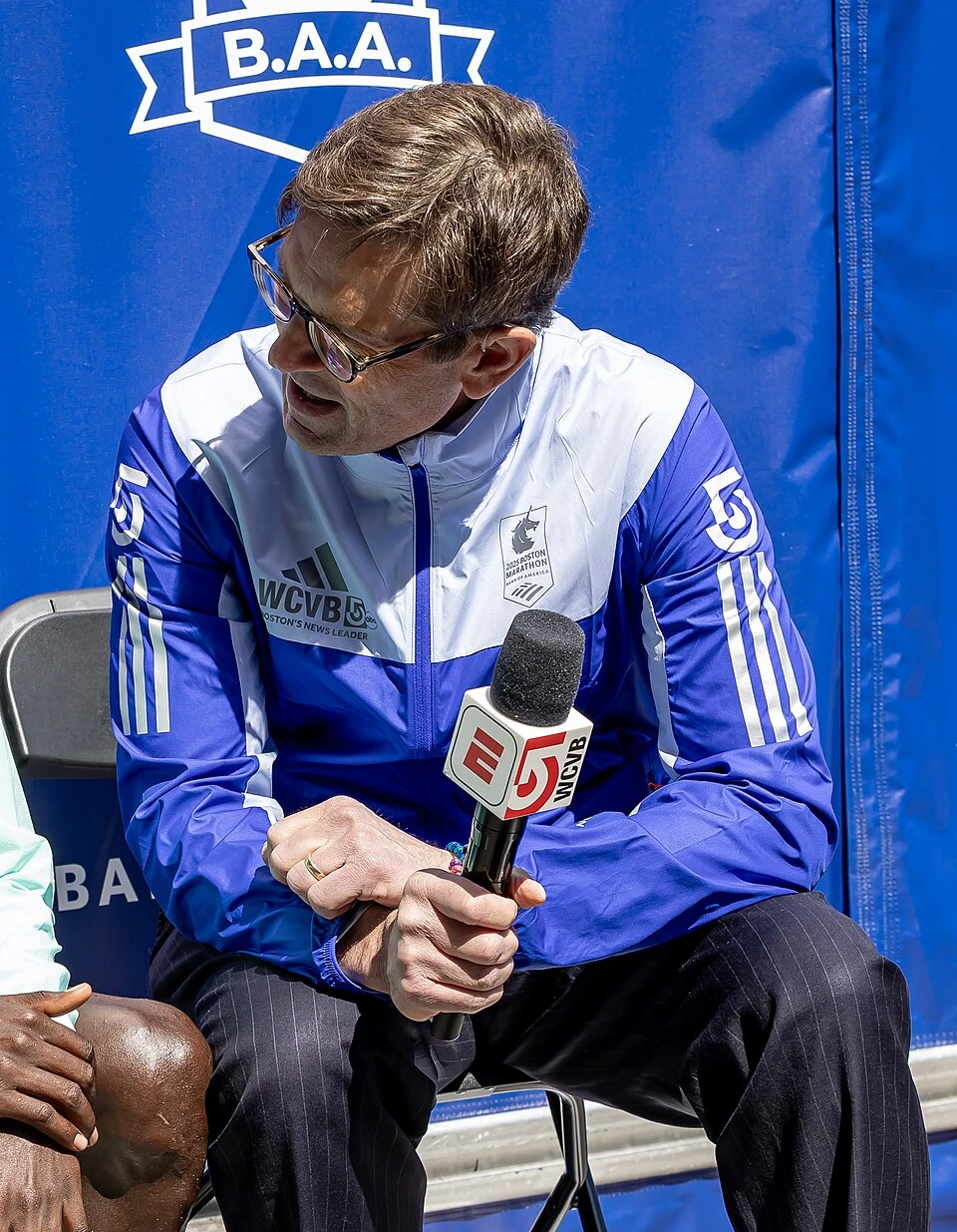 Duke Castiglione speaking into an NBC10 Boston microphone at a Boston Marathon event, wearing a WCVB-branded jacket