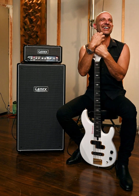 Constantine Delo seated beside a bass guitar and amplifier in a studio setting